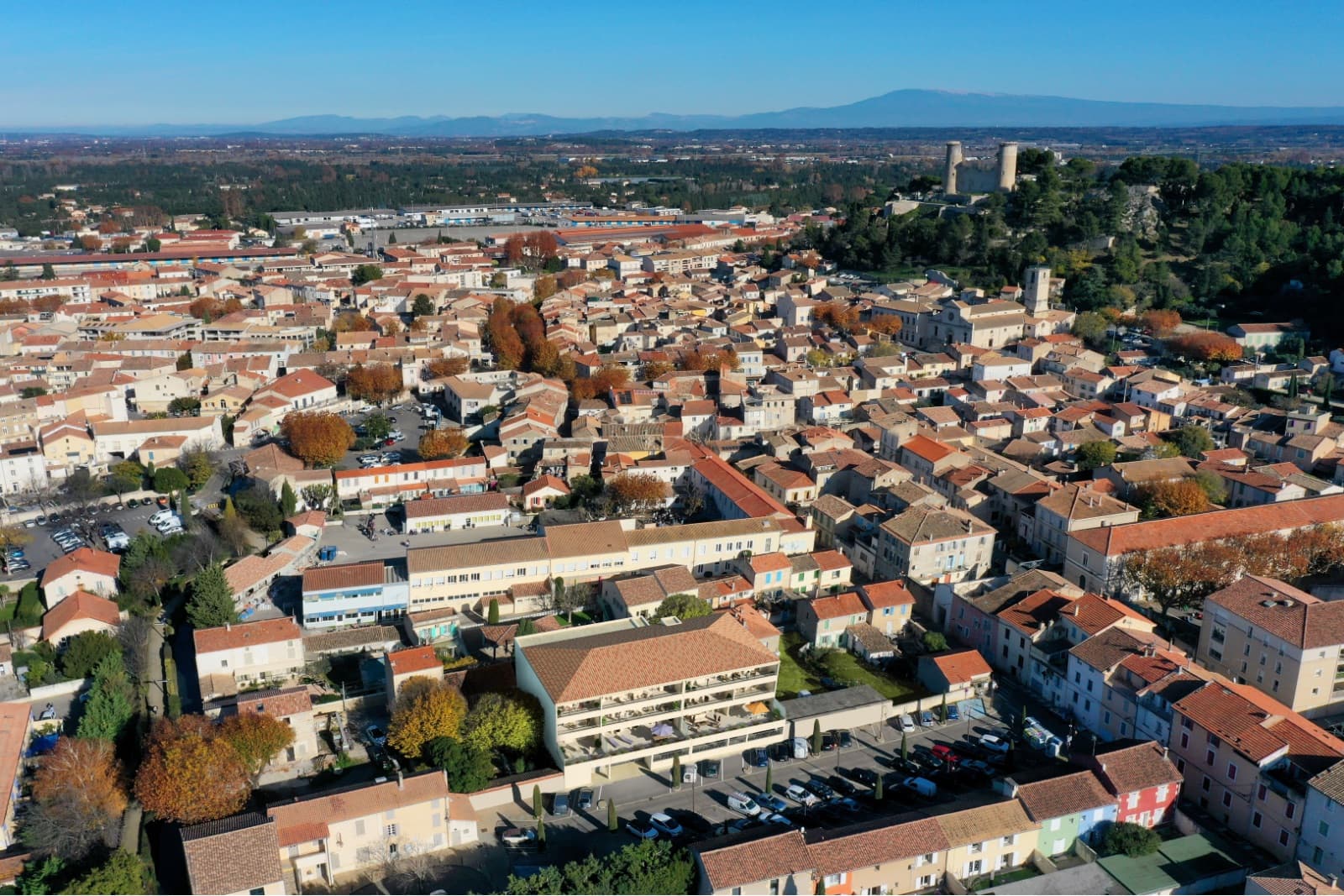 Vue aérienne de Châteaurenard: la résidence Cœur Castel insérée dans le tissu ancien du centre-ville, château des comtes de Provence et Ventoux à l'horizon.