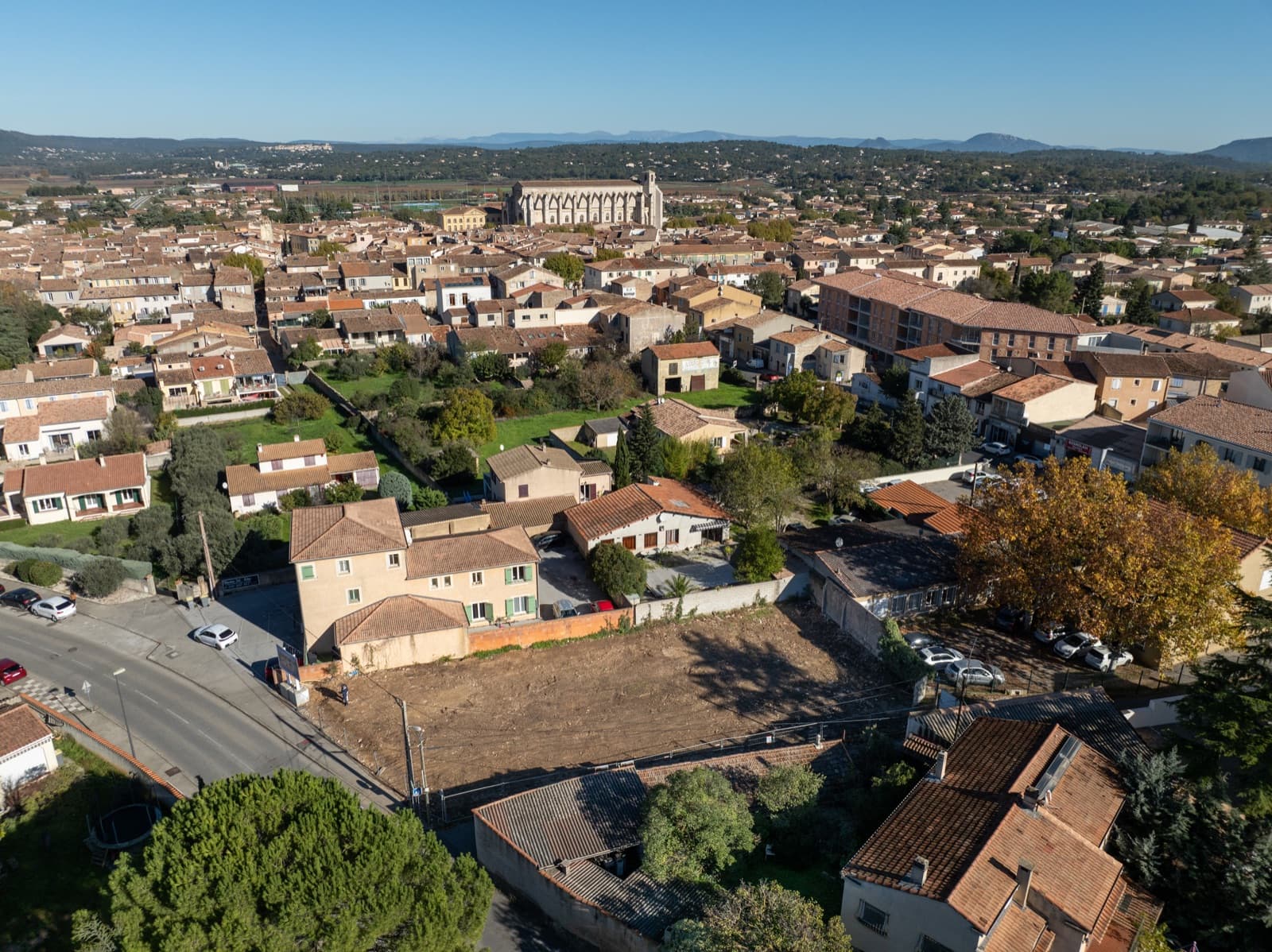 Vue aérienne de Saint-Maximin-la-Sainte-Baume: toits de tuiles du village autour de la basilique, collines de Provence à l'horizon.